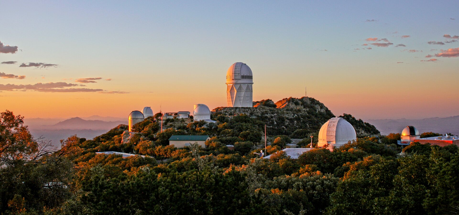Parte del Observatorio Nacional Kitt Peak. El Telescopio de 4 metros Nicholas U. Mayall se alza prominente en la cresta más alta. Este telescopio alberga el Instrumento Espectroscópico para el estudio de la Energía Oscura (DESI por sus siglas en inglés) que mide el efecto de la energía oscura en la expansión del Universo.