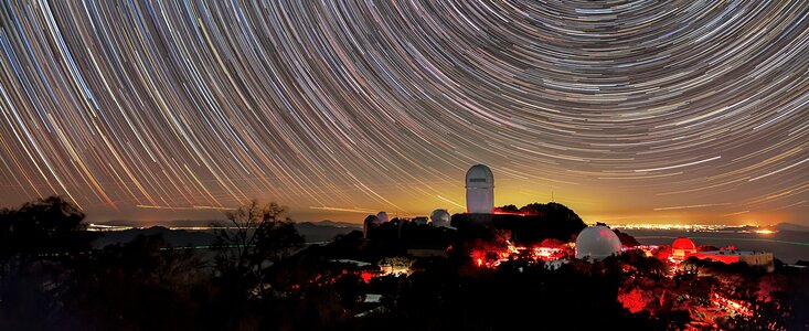 En esta fotografía (de exposición prolongada) se pueden ver senderos estelares en el Observatorio Nacional Kitt Peak, al igual que la distante contaminación lumínica de Tucson, Arizona (al fondo). La contaminación lumínica supone una amenaza creciente para los observatorios de investigación como Kitt Peak.