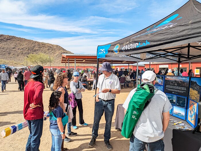 Los visitantes del Rodeo y Feria de la Nación Tohono O'odham de 2025 interactúan con voluntarios en el stand de información de NOIRLab de NSF.