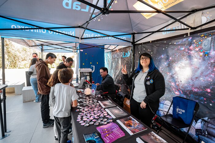 El ingeniero mecánico, Sebastián Olivares, y la guía de tours, Mackarena Órdenes, interactúan con estudiantes y familias en el stand de NOIRLab en el evento AstroDay Chile.